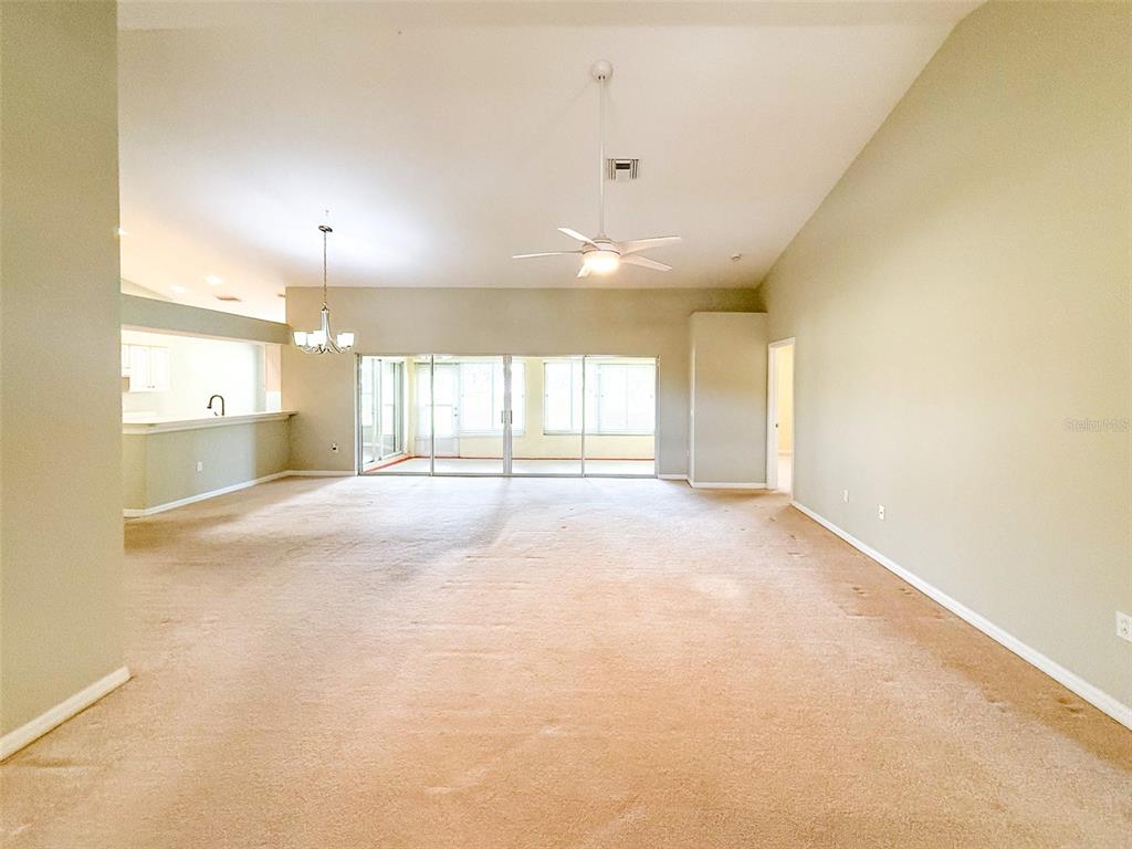 A spacious living room features beige carpeting, vaulted ceilings, a ceiling fan, and sliding glass doors — 18037 BAYWOOD FOREST DRIVE, HUDSON, FL