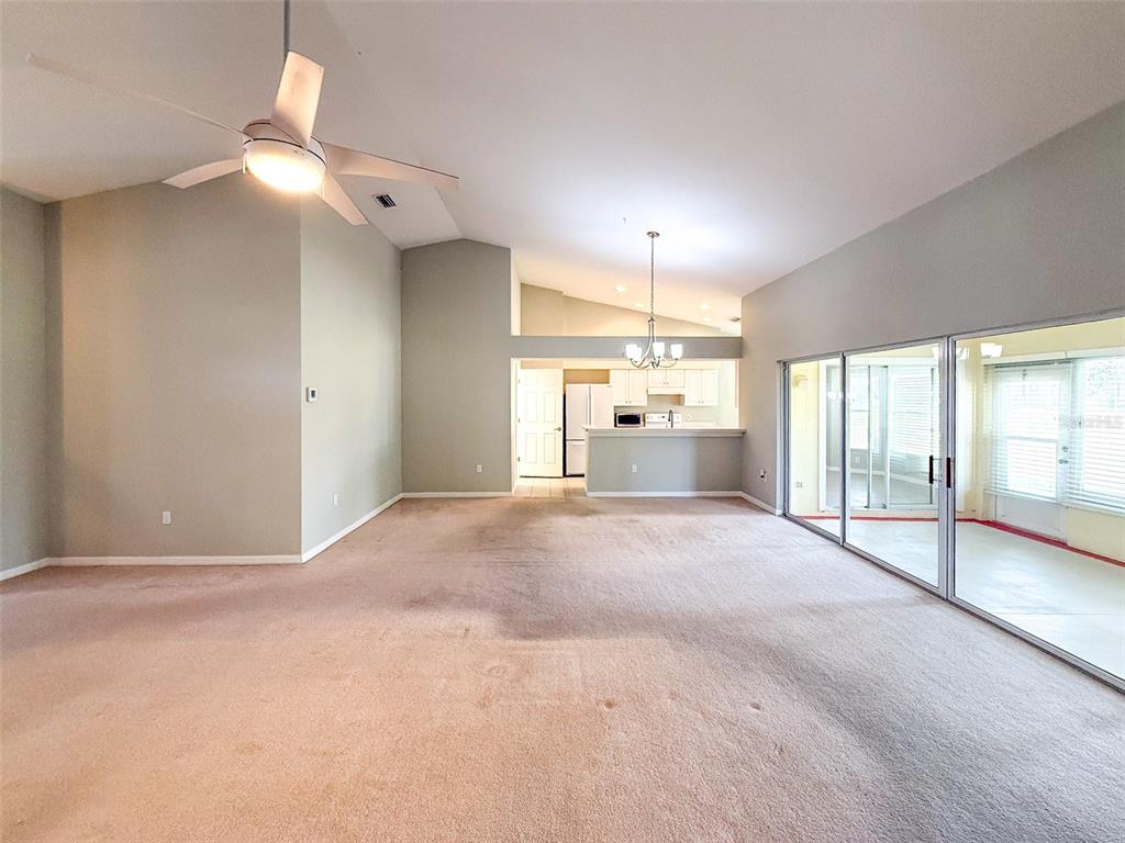 A spacious living room features beige carpeting, a vaulted ceiling, and sliding glass patio doors — 18037 BAYWOOD FOREST DRIVE, HUDSON, FL