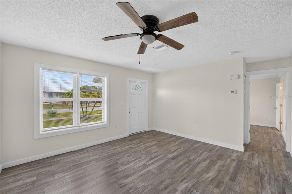 A living room with light-colored walls, wood-look flooring, a ceiling fan, and a front door — 5037 BULLARD STREET, NORTH PORT, FL