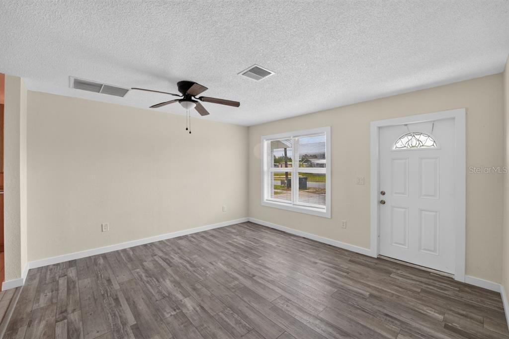 An empty room features light-colored walls, a ceiling fan, a window, and wood-look flooring — 5037 BULLARD STREET, NORTH PORT, FL