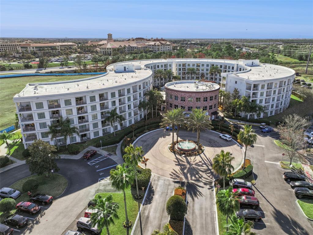 An aerial view shows a curved multi-story apartment building with a central fountain and parking — 225 CELEBRATION PLACE UNIT 526, KISSIMMEE, FL