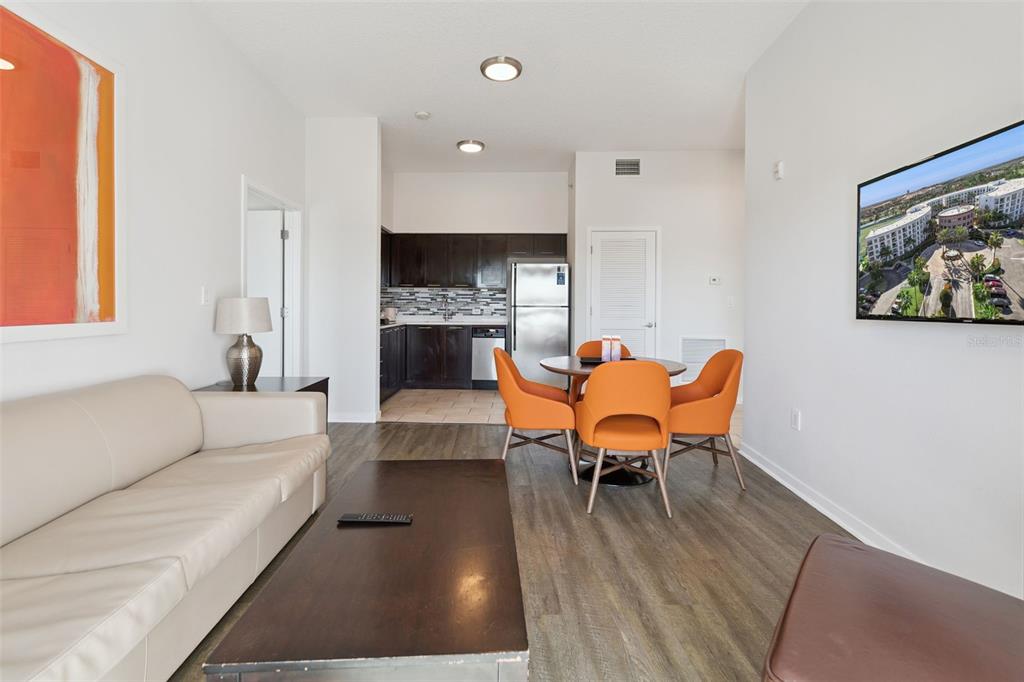 A living room and dining area with a kitchen, light flooring, and orange chairs — 225 CELEBRATION PLACE UNIT 526, KISSIMMEE, FL