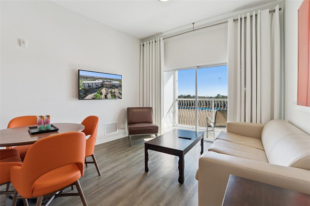 A living and dining area features orange chairs, a sofa, and a balcony with outdoor seating — 225 CELEBRATION PLACE UNIT 526, KISSIMMEE, FL