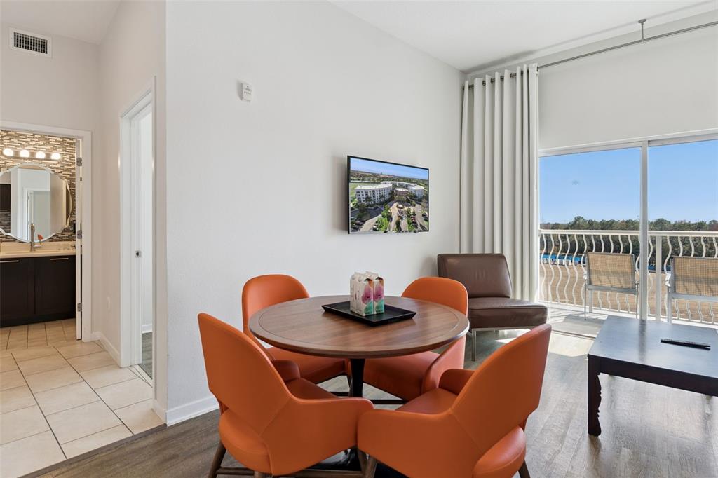 A dining area with orange chairs, a round table, and a balcony view — 225 CELEBRATION PLACE UNIT 526, KISSIMMEE, FL