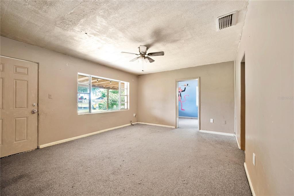 An empty living room features beige walls, gray carpeting, a ceiling fan, and a window — 124 CENTER STREET, WINTER HAVEN, FL