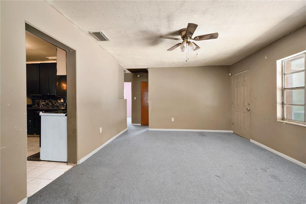 A living room with beige walls, gray carpeting, a ceiling fan, and an adjacent kitchen — 124 CENTER STREET, WINTER HAVEN, FL