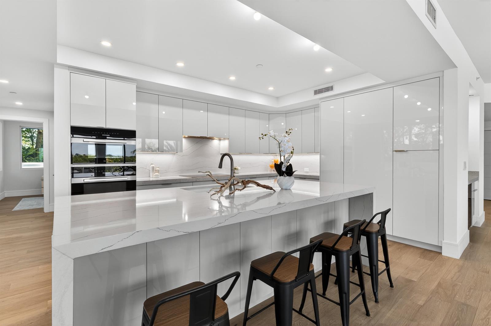 A modern kitchen features white glossy cabinets, a large quartz island, and three bar stools — 1 S Coastal Way # 201, Jupiter FL 33477, JUPITER, FL
