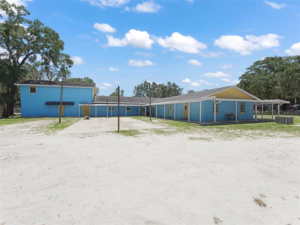 A long, blue, single-story building with a covered porch sits on a sandy lot — 9475 SE 35TH COURT, OCALA, FL