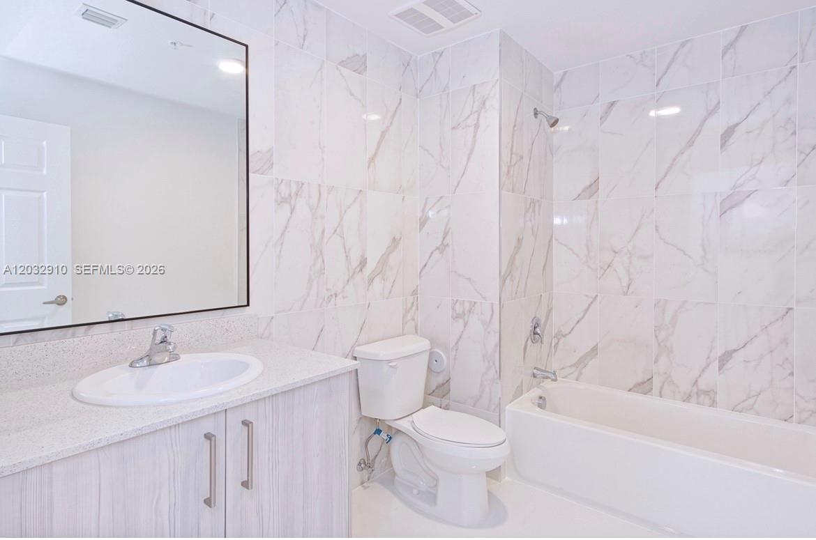 A bathroom features a white vanity, a toilet, and a bathtub with marble-patterned wall tiles — 10950 NW 82nd St # 207, Doral FL 33178, DORAL, FL
