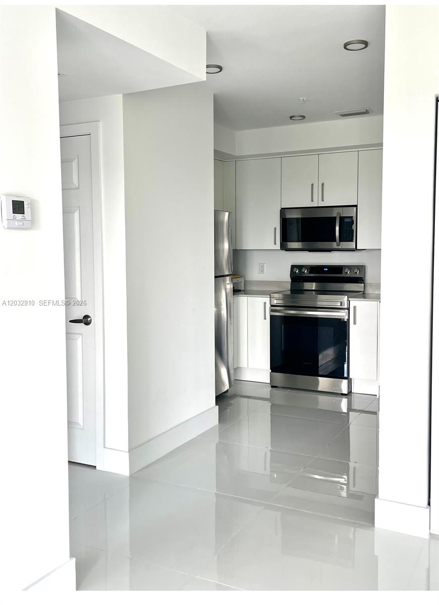A kitchen features white cabinets, stainless steel appliances, and glossy light-colored floor tiles — 10950 NW 82nd St # 207, Doral FL 33178, DORAL, FL