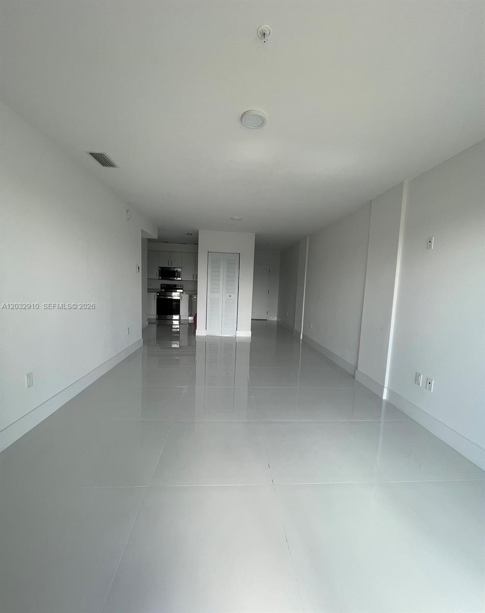 An empty room with white walls, glossy tile flooring, and a view of the kitchen — 10950 NW 82nd St # 207, Doral FL 33178, DORAL, FL