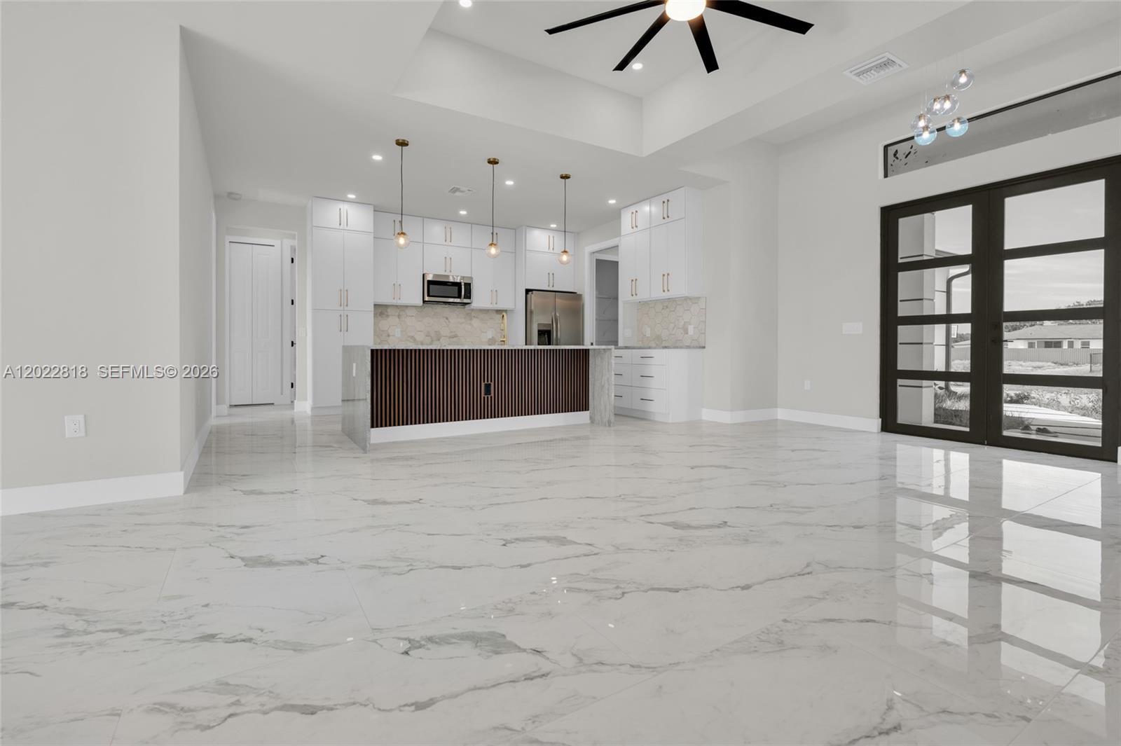 A modern kitchen features white cabinetry, a slatted wood island, and polished marble-look flooring — 1413 NE 4TH PL, Cape Coral FL 33909, CAPE CORAL, FL