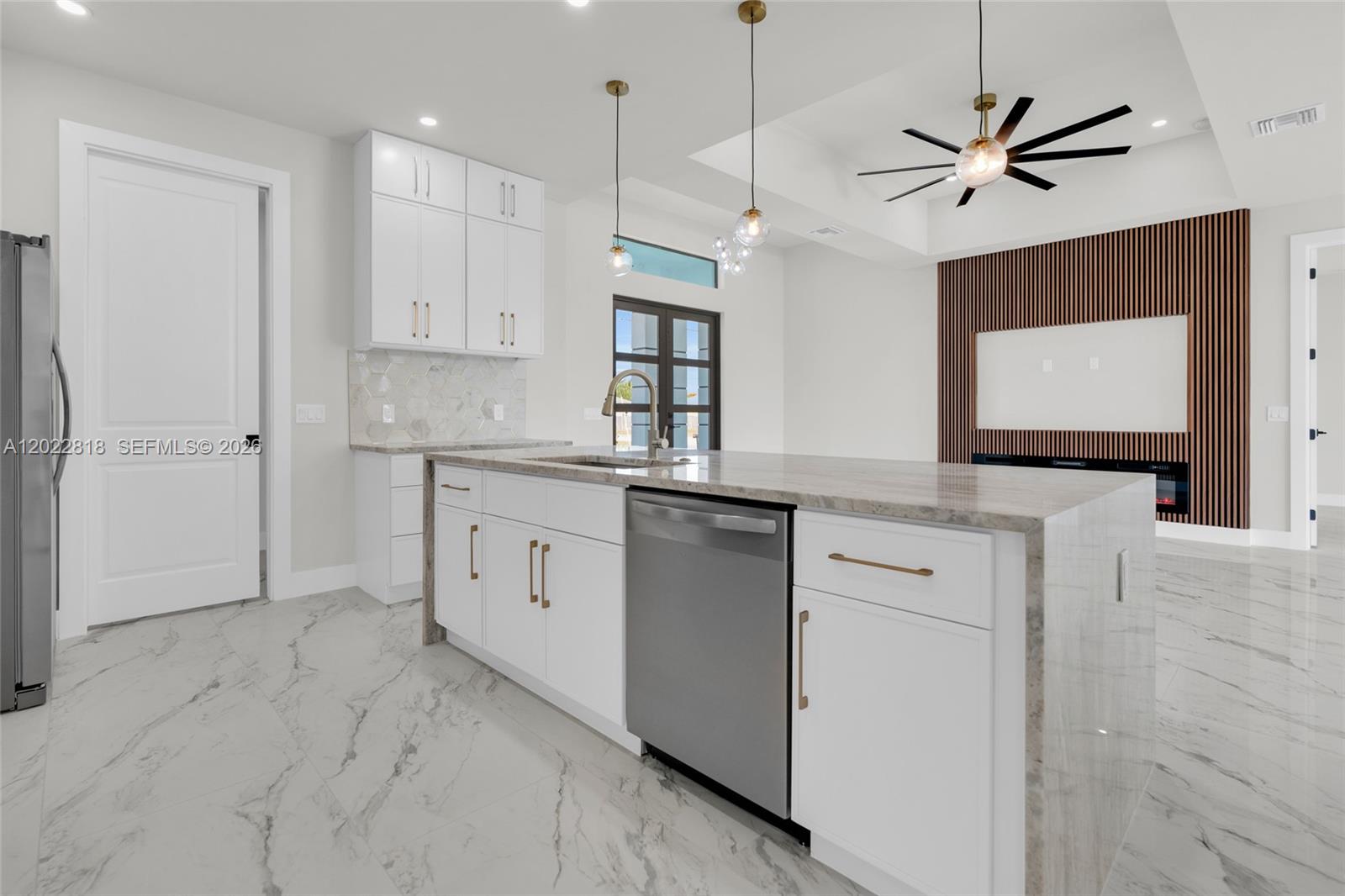 A modern kitchen features white cabinetry, a marble-topped island, and a wood-slat accent wall — 1413 NE 4TH PL, Cape Coral FL 33909, CAPE CORAL, FL