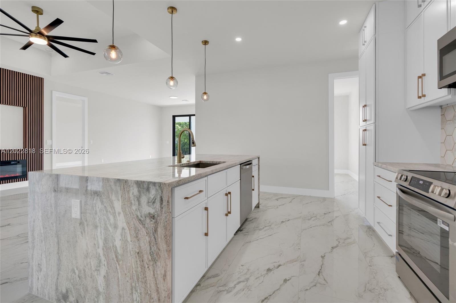 A modern kitchen features a large marble island, white cabinetry, and gold hardware — 1413 NE 4TH PL, Cape Coral FL 33909, CAPE CORAL, FL