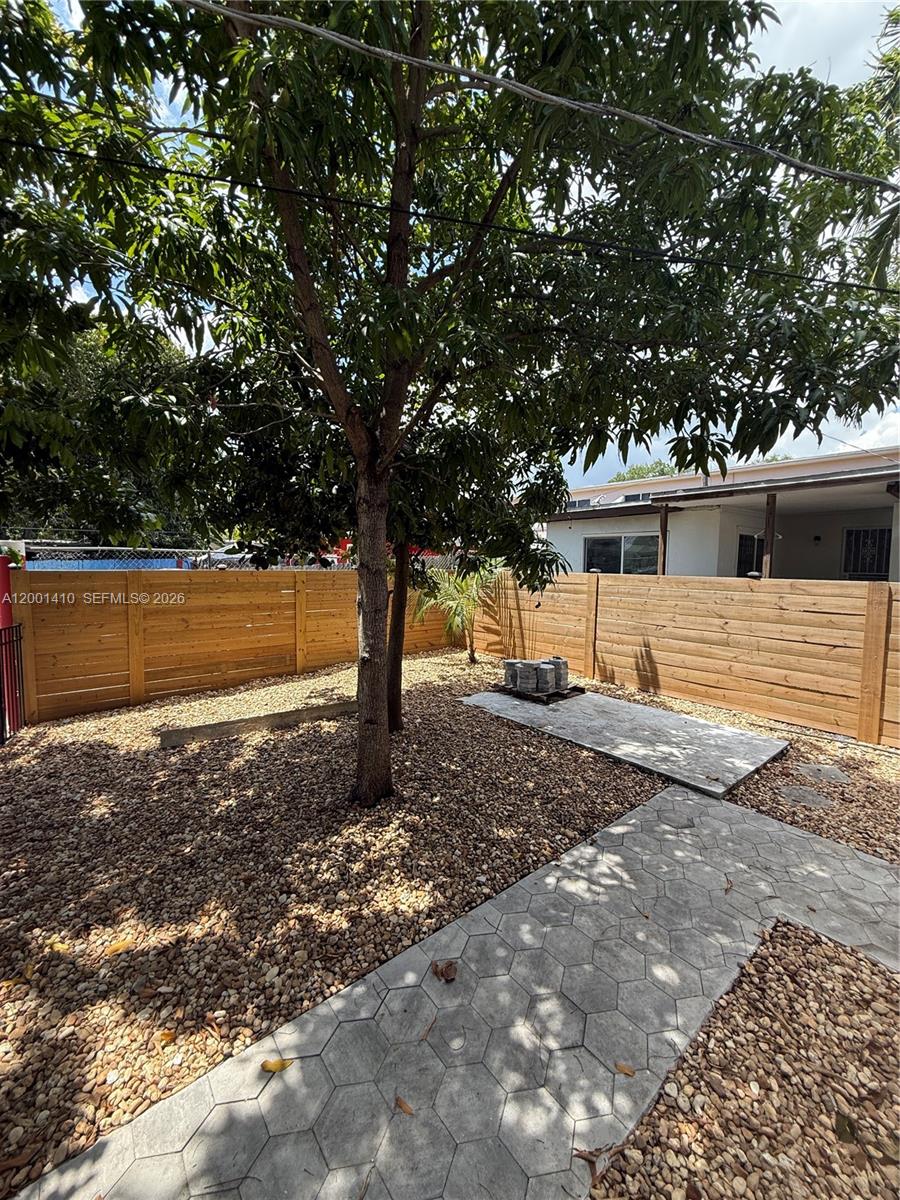 A fenced backyard features a gravel ground cover, a concrete patio, and a large tree — 5530 NW Miami Ct, Miami FL 33127, MIAMI, FL