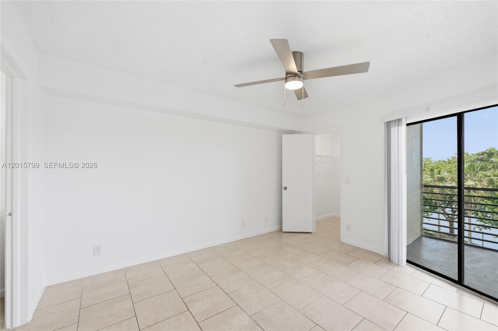 An empty bedroom features white walls, tile flooring, a ceiling fan, and a balcony door — SUNRISE, FL