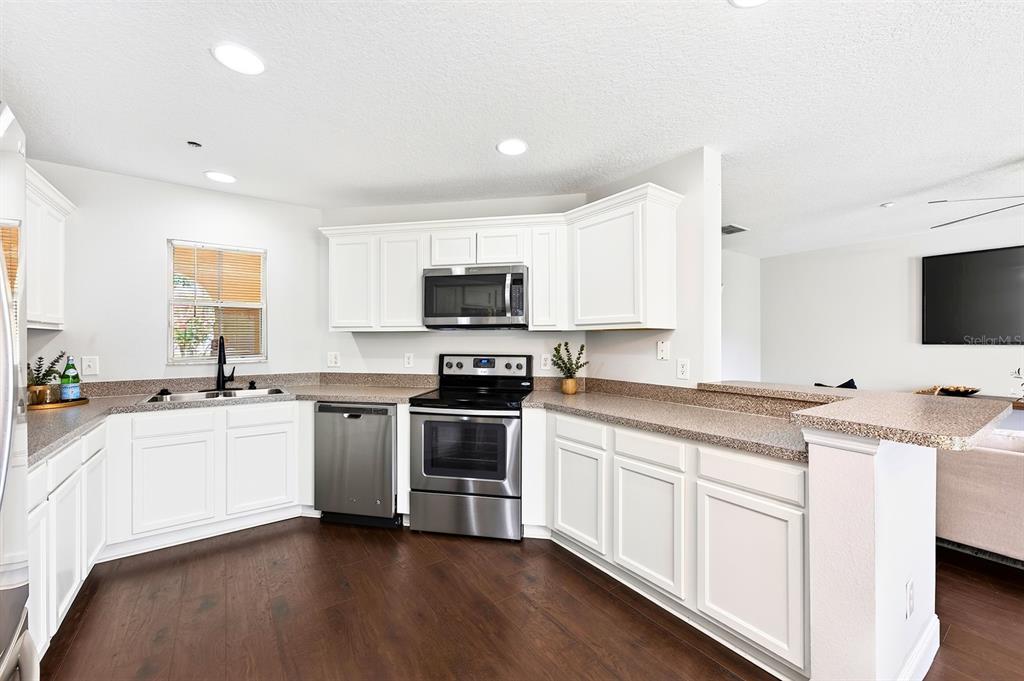 A kitchen features white cabinets, stainless steel appliances, and brown countertops over dark wood flooring — 13765 GOLDEN RUSSET DRIVE, WINTER GARDEN, FL