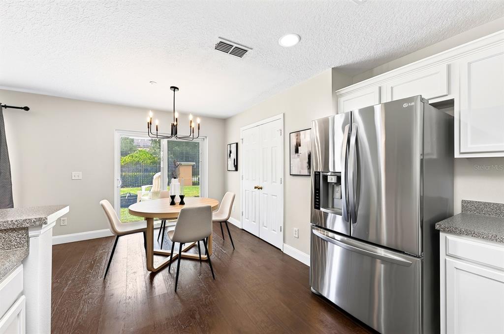 A dining area features a round wooden table, modern chairs, and a stainless steel refrigerator — 13765 GOLDEN RUSSET DRIVE, WINTER GARDEN, FL