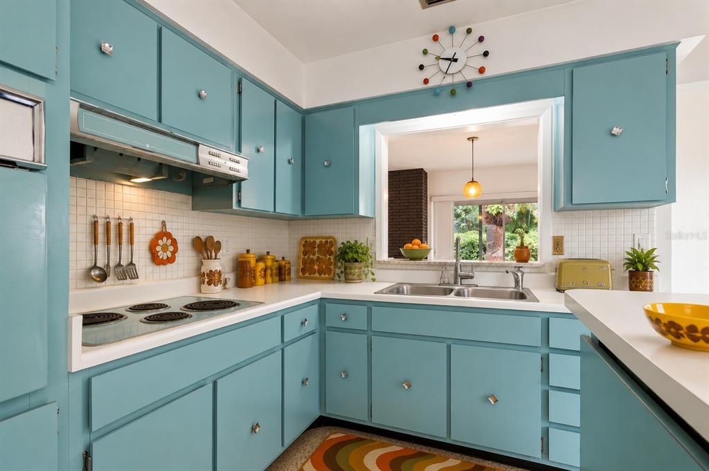 A kitchen with blue cabinets, a white tiled backsplash, and a pass-through window to outside — 243 3RD STREET W, TIERRA VERDE, FL