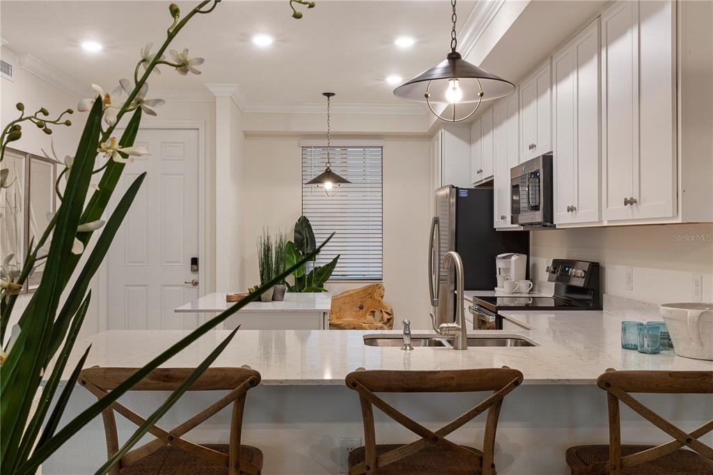 A kitchen with white cabinets, quartz countertops, stainless steel appliances, and wooden bar stools — 17510 GAWTHROP DRIVE UNIT 104, BRADENTON, FL