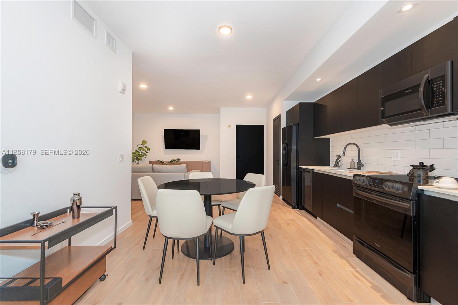 A modern kitchen and dining area features black cabinetry, white subway tile, and light wood flooring — 398 NE 5th St # 4417, Miami FL 33132, MIAMI, FL