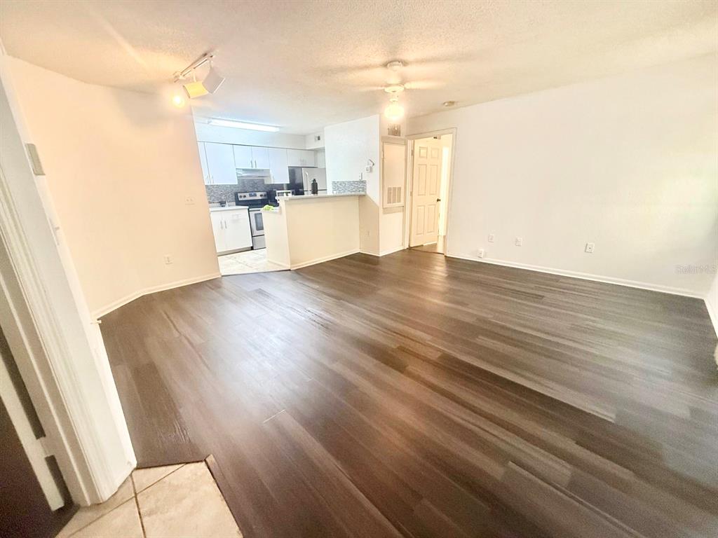 An open-concept living area features dark wood-look flooring and an adjacent kitchen with white cabinets — 2201 METROPOLITAN WAY UNIT 1423, ORLANDO, FL