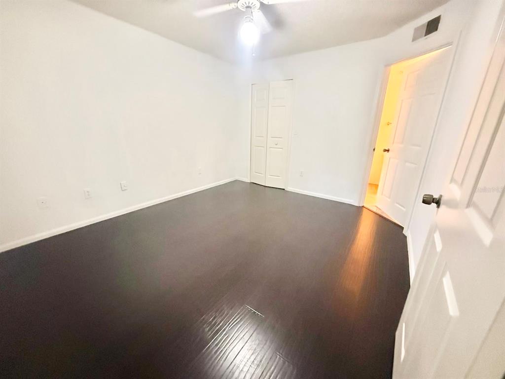 An empty bedroom features dark wood-look flooring, white walls, a ceiling fan, and a closet — 2201 METROPOLITAN WAY UNIT 1423, ORLANDO, FL