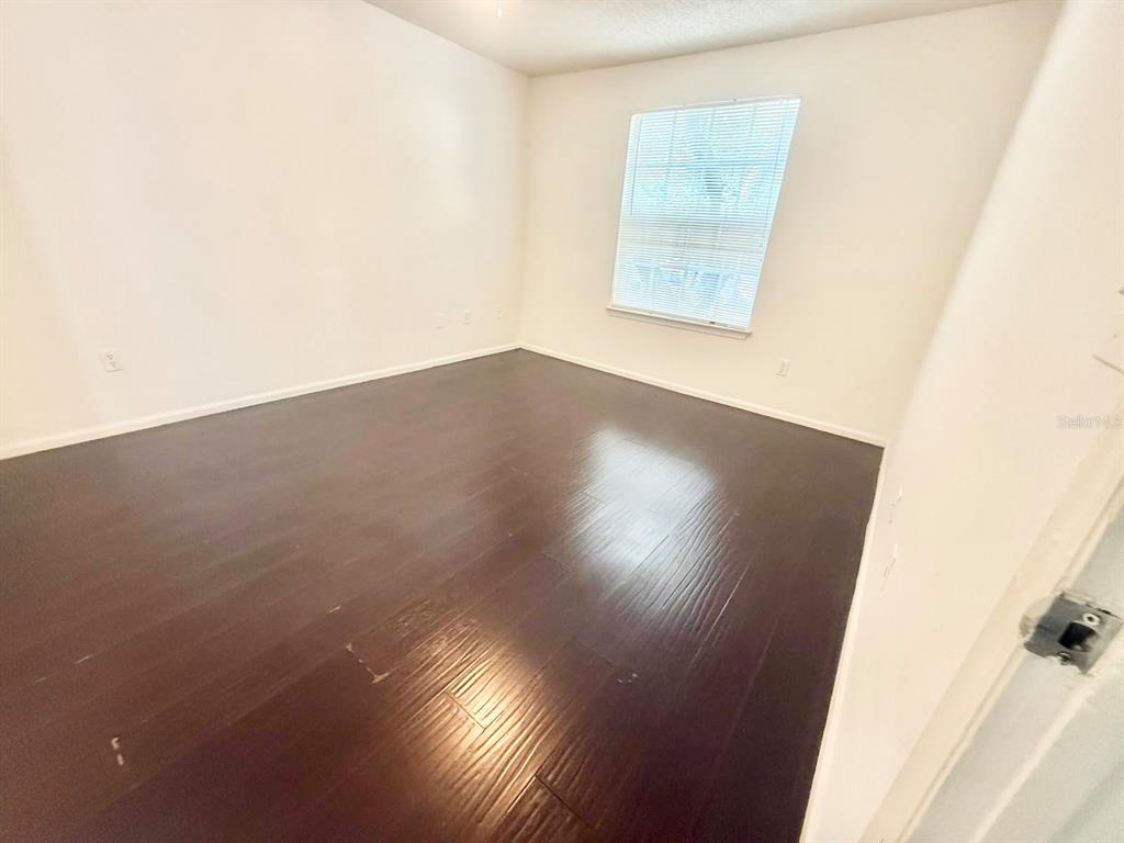An empty bedroom features dark wood-look flooring, white walls, and a single window with blinds — 2201 METROPOLITAN WAY UNIT 1423, ORLANDO, FL