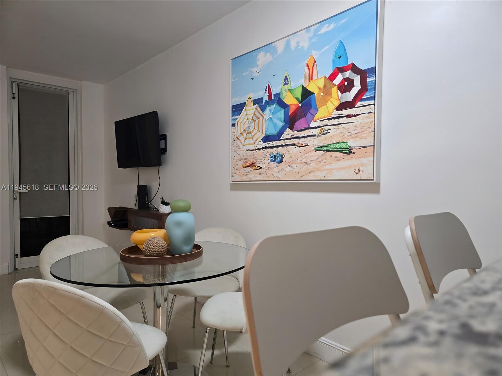 A dining area features a glass-topped table, white chairs, and a large beach-themed wall painting — 100 Lincoln Rd # 503, Miami Beach FL 33139, MIAMI BEACH, FL