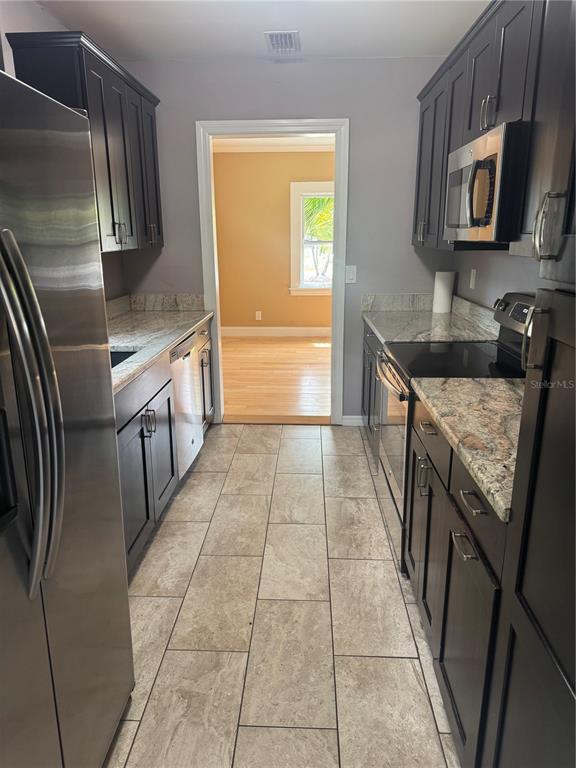 A galley kitchen features dark cabinets, granite countertops, stainless steel appliances, and tiled flooring — 1701 53RD STREET S, GULFPORT, FL
