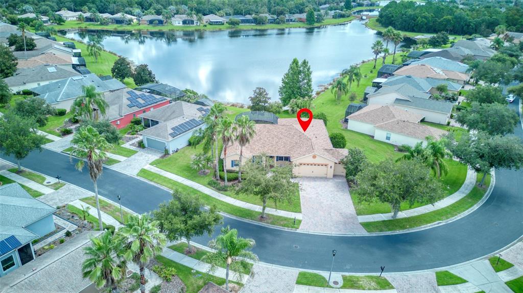 An aerial view shows a suburban house with a tan roof situated near a lake — 392 DAVINCI PASS, POINCIANA, FL