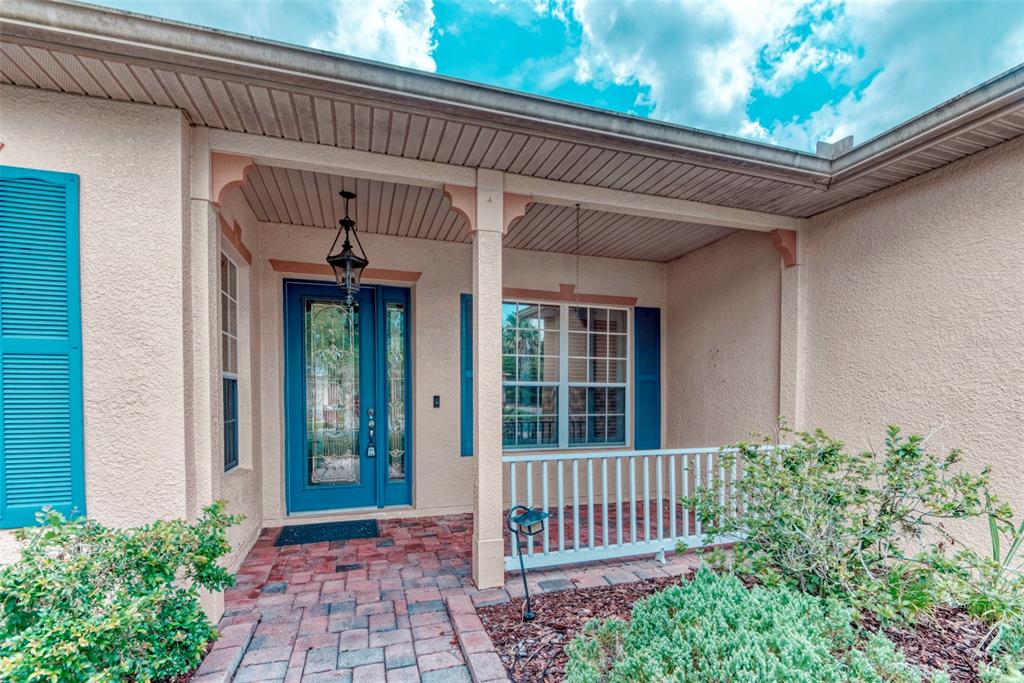 A front porch with a blue door, brick walkway, and white railing against a stucco exterior — 392 DAVINCI PASS, POINCIANA, FL
