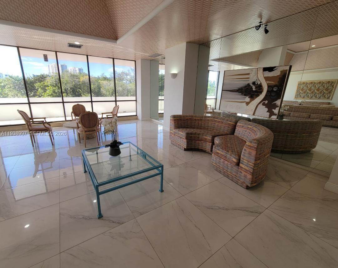 A living room features marble floors, a glass coffee table, and a curved patterned sofa — 500 Three Islands Blvd # 709, Hallandale Beach FL 33009, HALLANDALE BEACH, FL