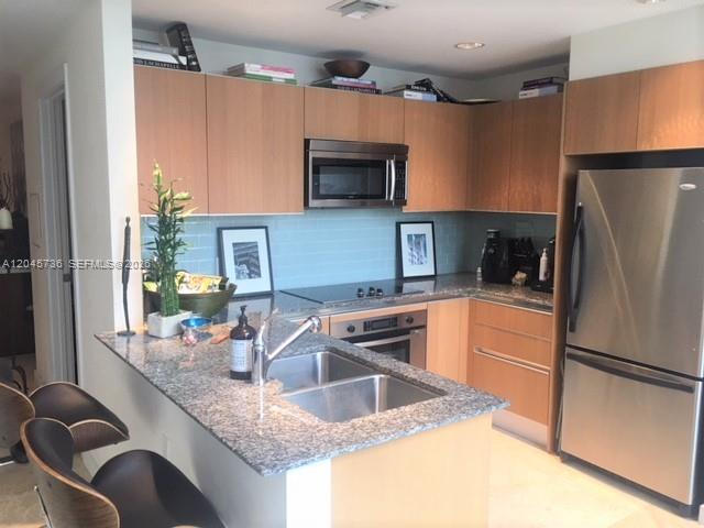A modern kitchen features light wood cabinets, granite countertops, stainless steel appliances, and bar seating — MIAMI, FL