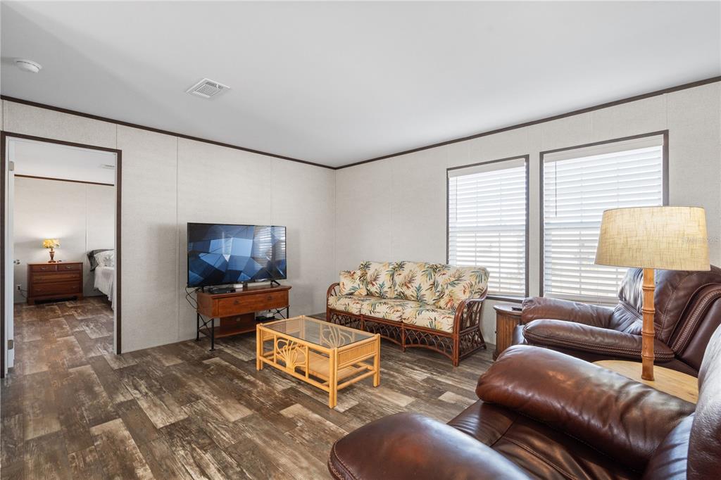 A living room with a beige sofa, wicker chair, blue armchair, and a television console — 224 WOLVERINE AVENUE, NORTH PORT, FL