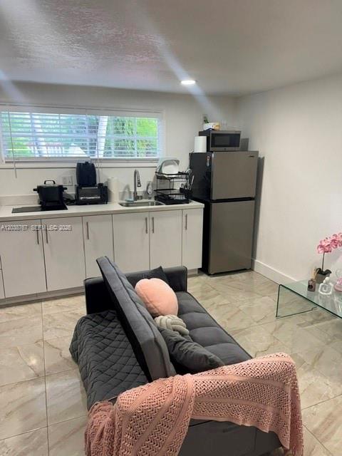 A small kitchen with white cabinets and stainless steel appliances sits behind a gray sofa — 211 SW 71st Ave, Miami FL 33144, MIAMI, FL