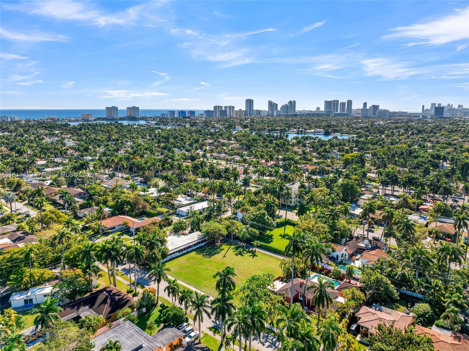 An aerial view shows a residential neighborhood with lush trees, swimming pools, and a distant skyline — 1310 Polk St, Hollywood FL 33019, HOLLYWOOD, FL