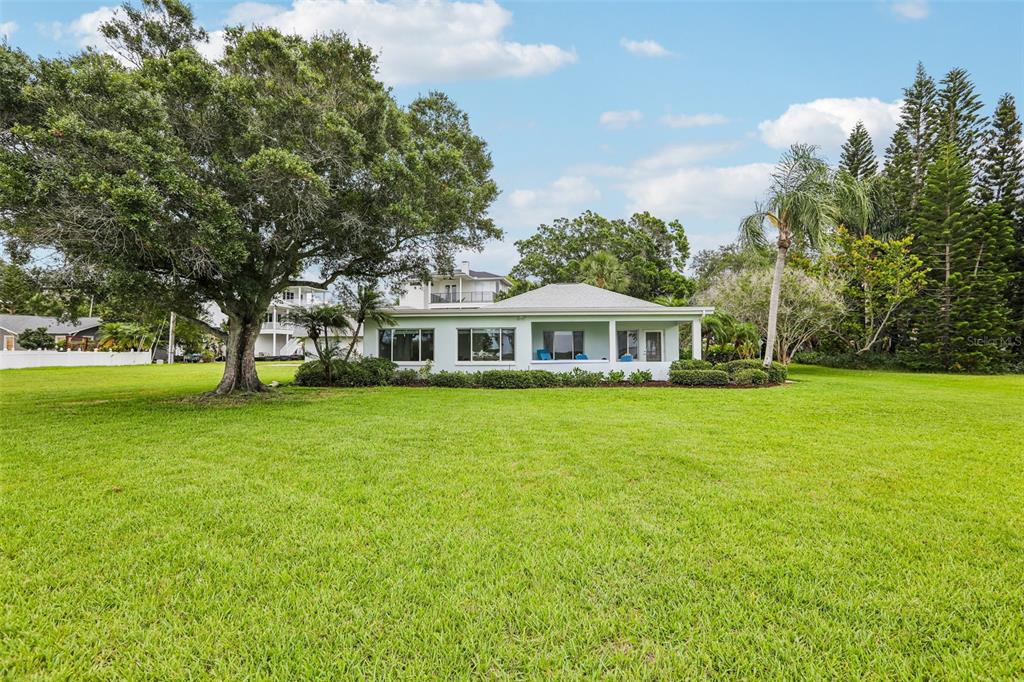 A light-colored house with a covered porch sits behind a large, expansive green lawn — 610 INDIANA AVENUE, CRYSTAL BEACH, FL