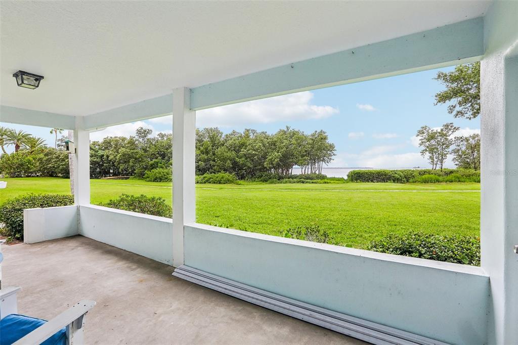 A covered porch with light blue walls overlooks a grassy lawn and a distant body of water — 610 INDIANA AVENUE, CRYSTAL BEACH, FL