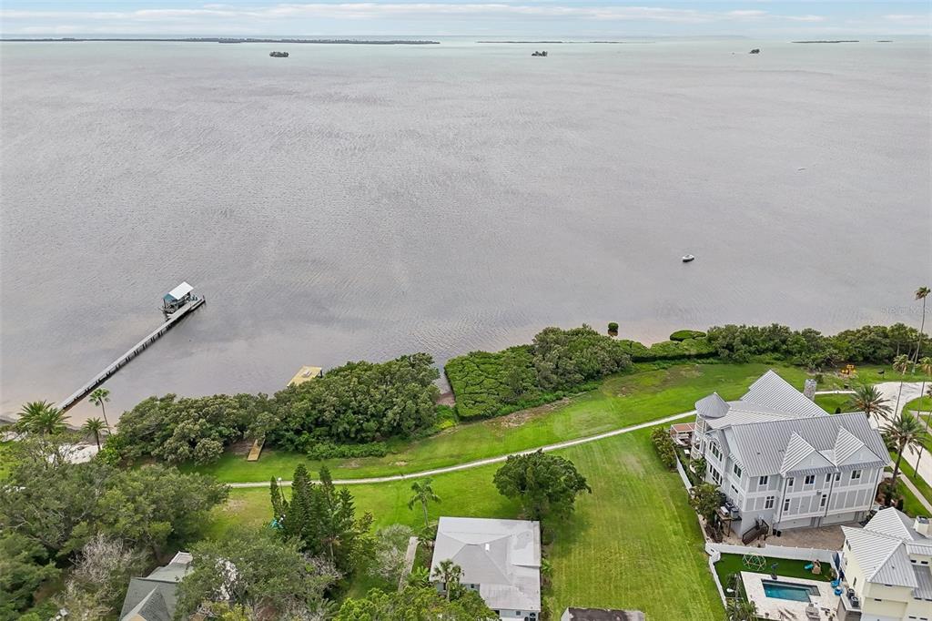 An aerial view shows a waterfront property with a long dock, green lawn, and houses — 610 INDIANA AVENUE, CRYSTAL BEACH, FL