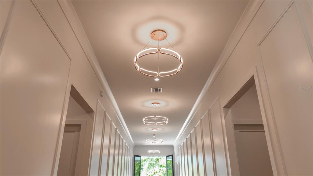 A long, white-walled hallway features three modern, circular pendant lights and paneled wall details — 1220 DELANEY PARK DRIVE, ORLANDO, FL