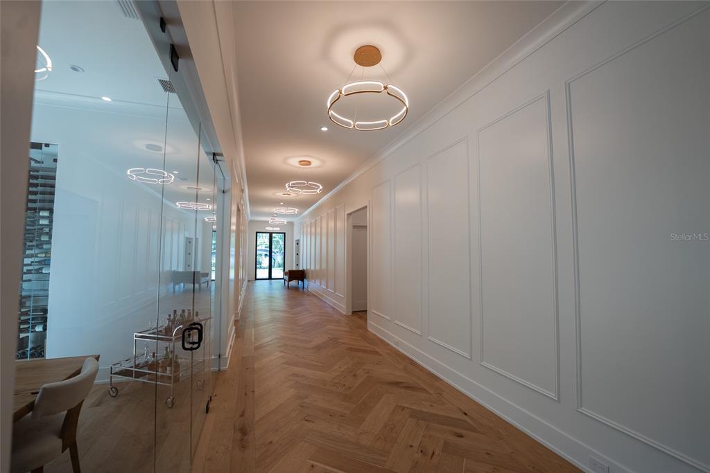 A long hallway with herringbone wood floors, white paneled walls, and modern circular light fixtures — 1220 DELANEY PARK DRIVE, ORLANDO, FL