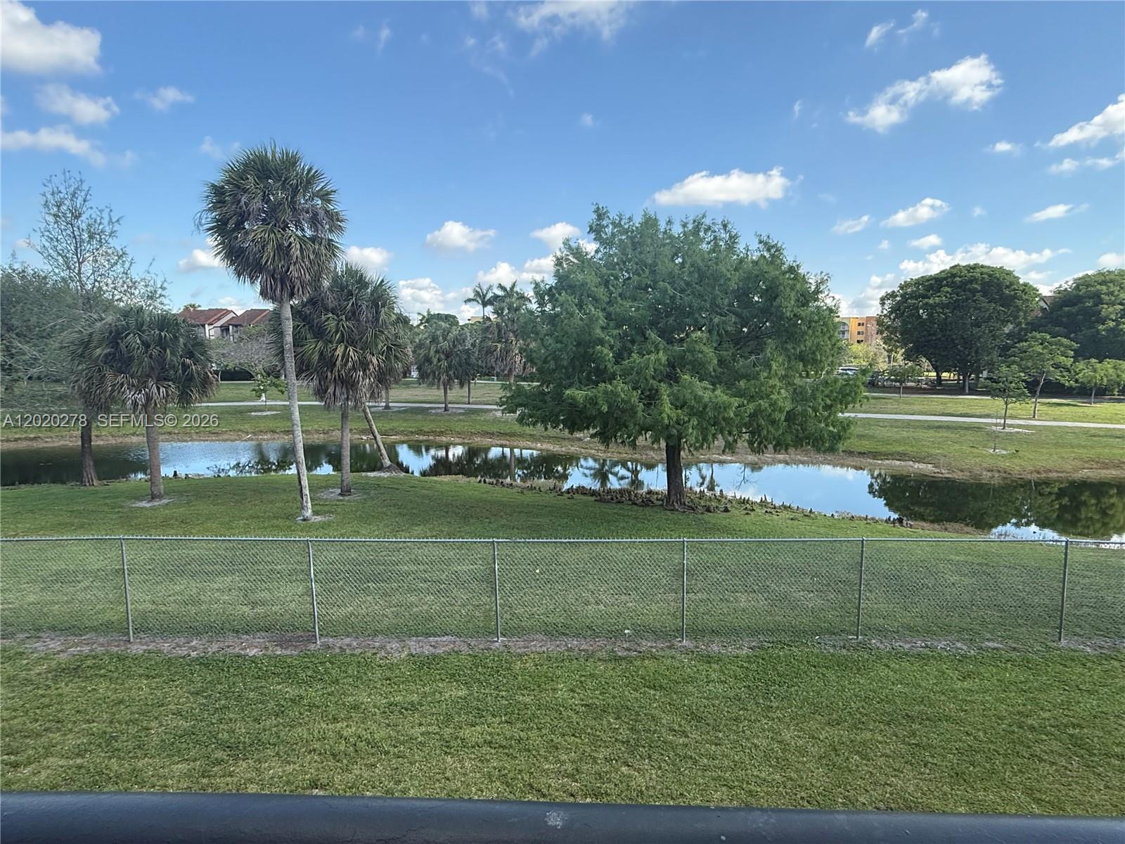 A chain-link fence overlooks a grassy lawn, a small pond, and several trees — 7195 NW 179th St, Hialeah FL 33015, HIALEAH, FL