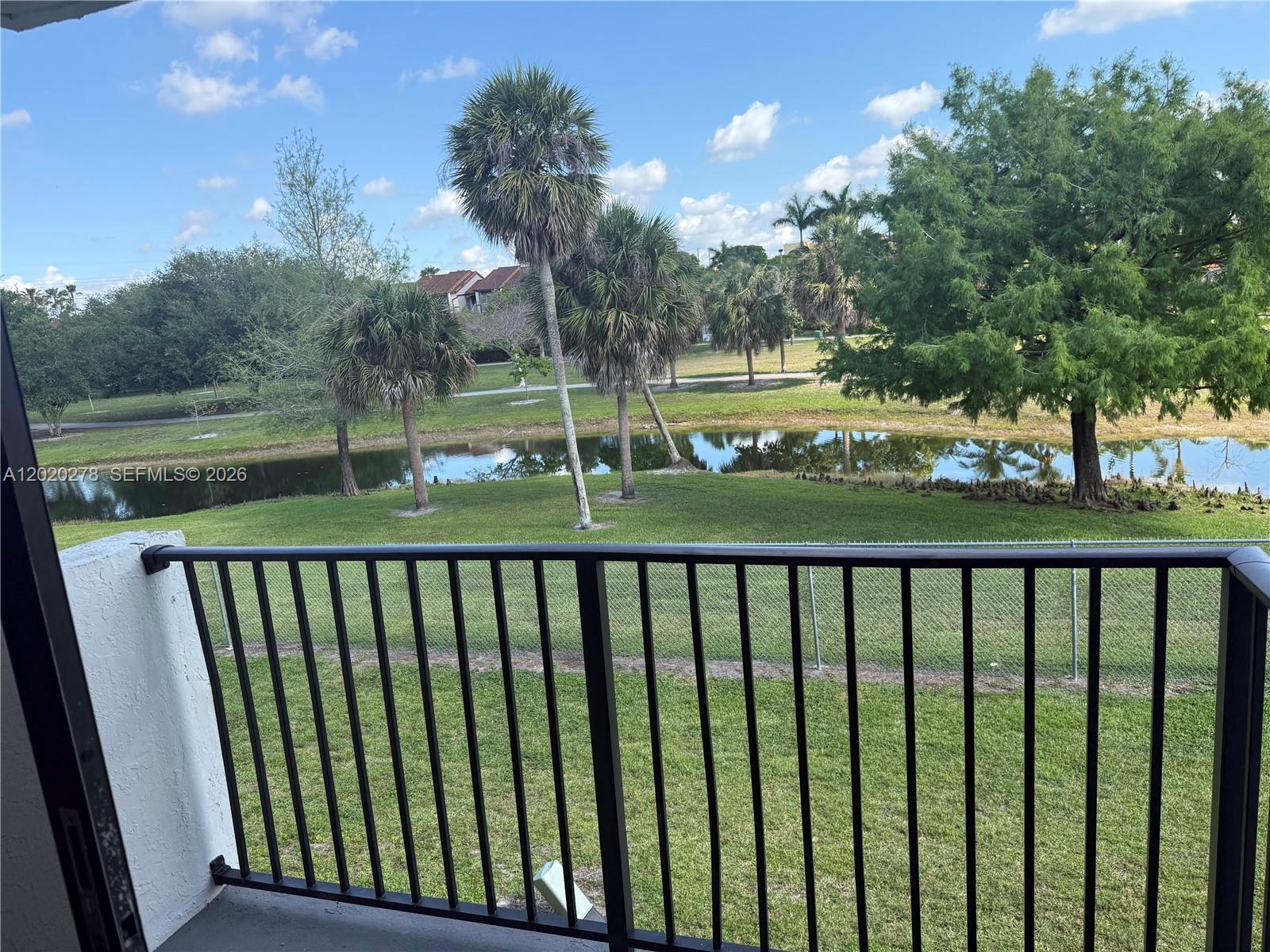 A balcony with a black metal railing overlooks a grassy lawn, pond, and palm trees — 7195 NW 179th St, Hialeah FL 33015, HIALEAH, FL