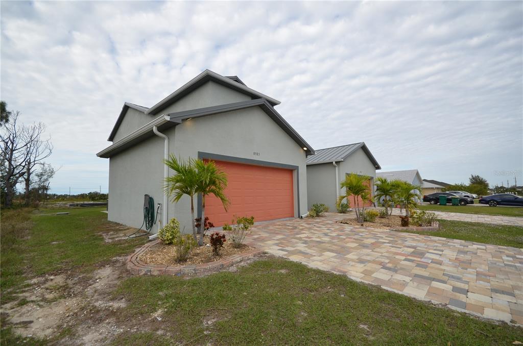 A gray house with an orange garage door and a paved driveway under a cloudy sky — 8581 AGATE STREET, PORT CHARLOTTE, FL