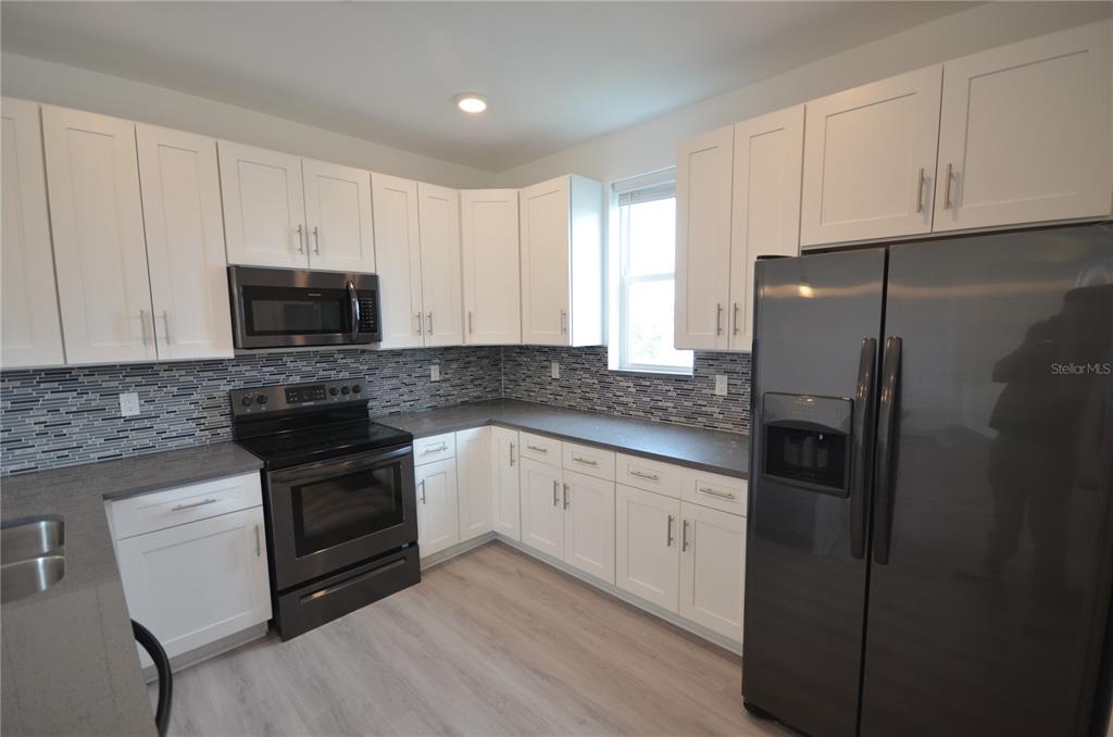 A kitchen features white cabinets, dark countertops, a tiled backsplash, and stainless steel appliances — 8581 AGATE STREET, PORT CHARLOTTE, FL