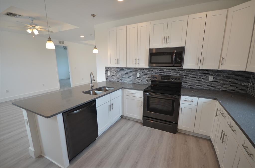 A kitchen features white cabinets, dark countertops, a tiled backsplash, and black appliances — 8581 AGATE STREET, PORT CHARLOTTE, FL