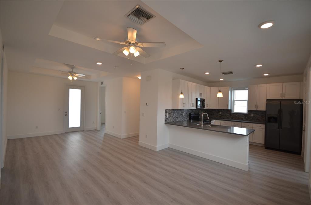 An open-concept kitchen and living area with white cabinets, dark countertops, and light wood flooring — 8581 AGATE STREET, PORT CHARLOTTE, FL