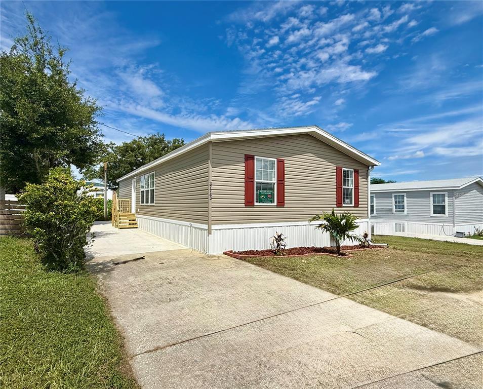 A tan manufactured home with red shutters and a concrete driveway under a blue sky — 37743 GEIGER ROAD, ZEPHYRHILLS, FL