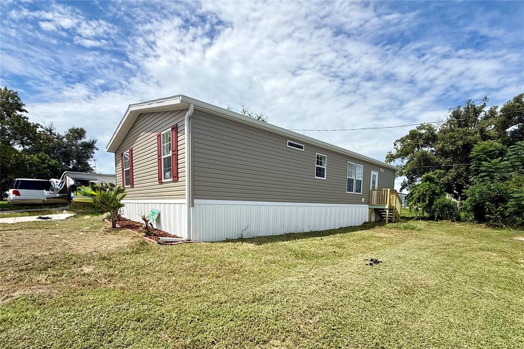 A tan manufactured home with white skirting and red window shutters sits on a lawn — 37743 GEIGER ROAD, ZEPHYRHILLS, FL